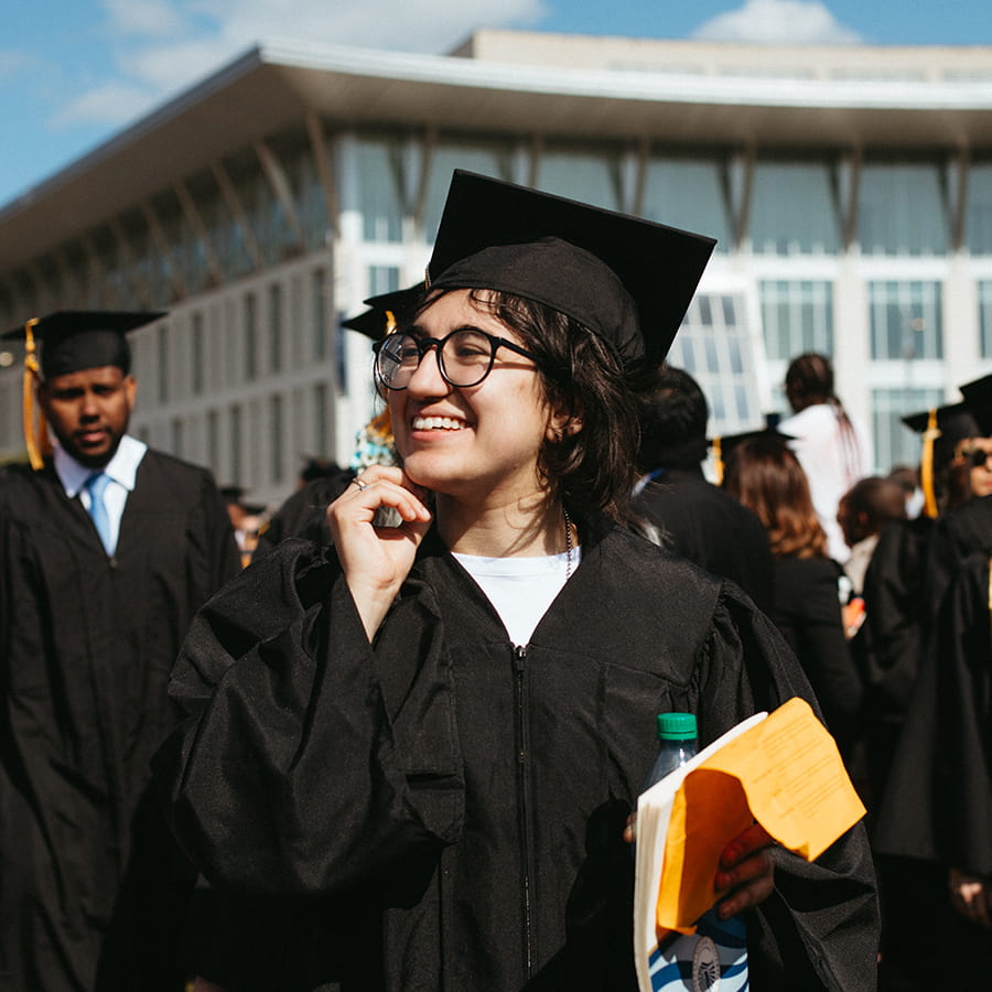 Student in cap & gown at commencement on Campus Center lawn.