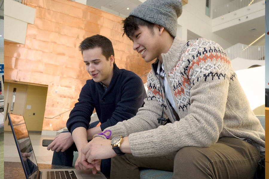 2 Students look at laptop on bench in University Hall.