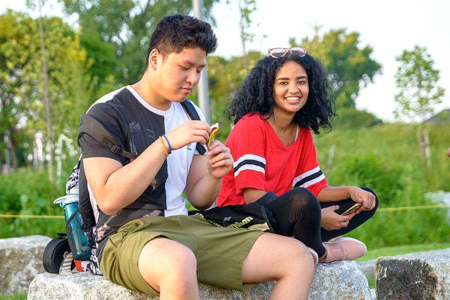 Two students sit outside on stone benches.