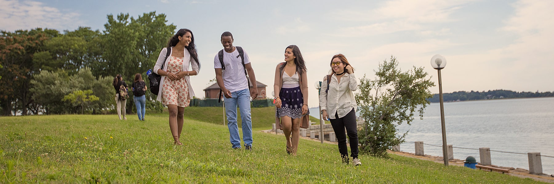 4 students walk along the lawn by the water.