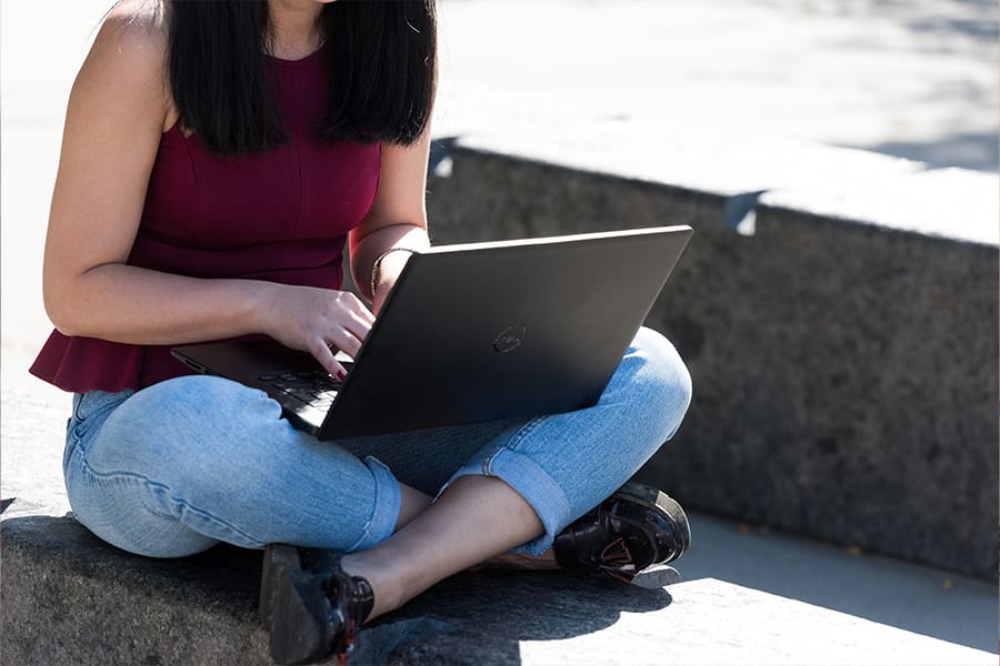 Student types on laptop outside.