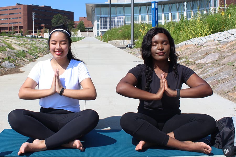 2 students do yoga campus center lawn.