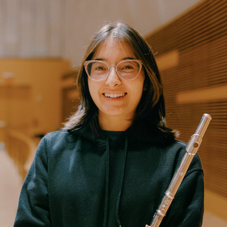 Mya-Jai holds flute smiling in the auditorium.