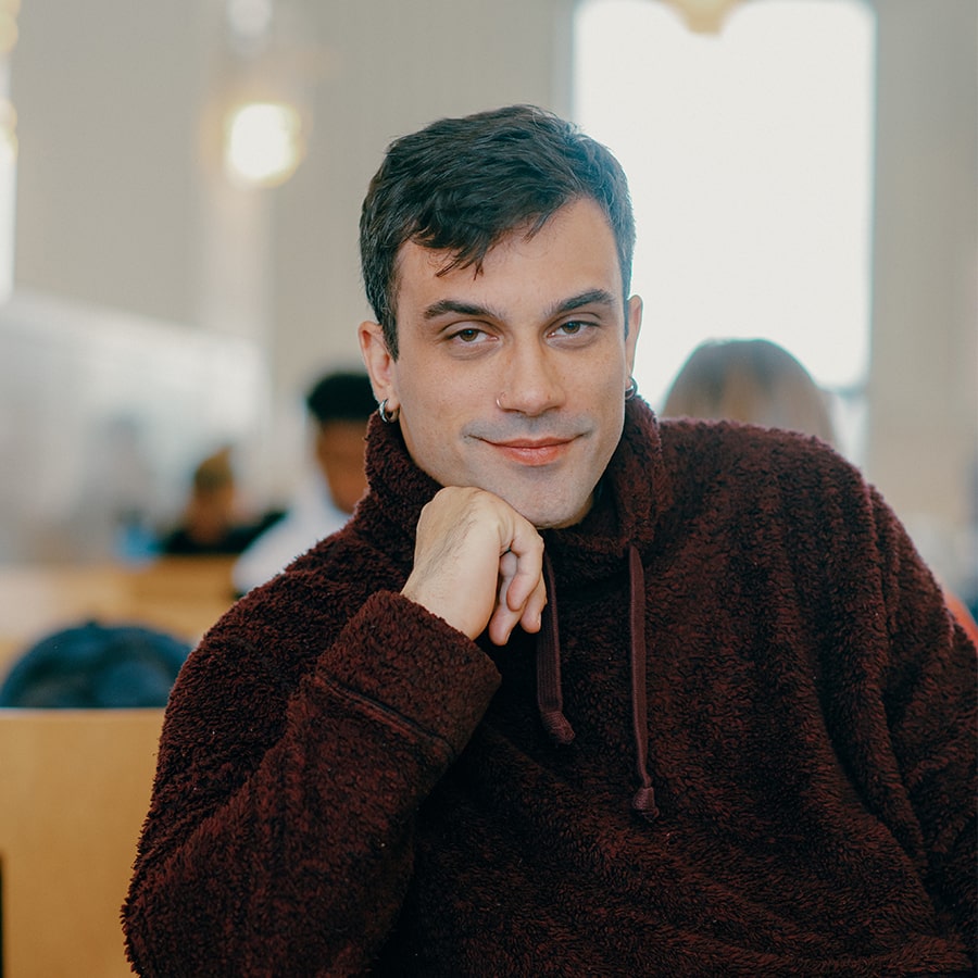 Stefan sits in the cafeteria looking thoughtfully at camera.