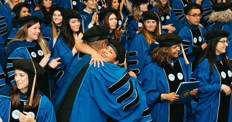 doctoral candidates hug at the hooding ceremony