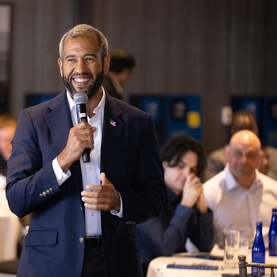 bearded man in casual business attire with american flag on lapel with microphone at Best Boston networking event