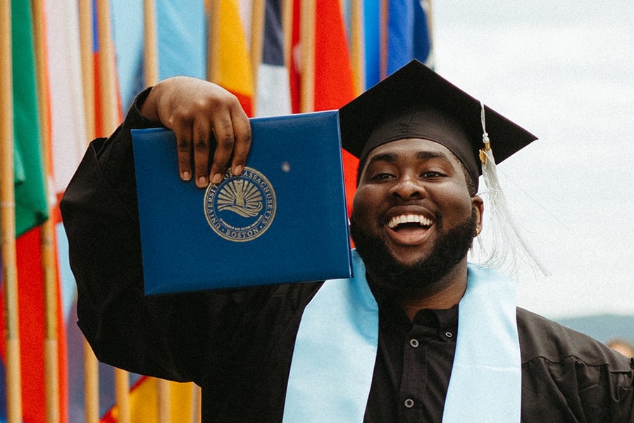 student wearing graduation cap holds diploma in hand